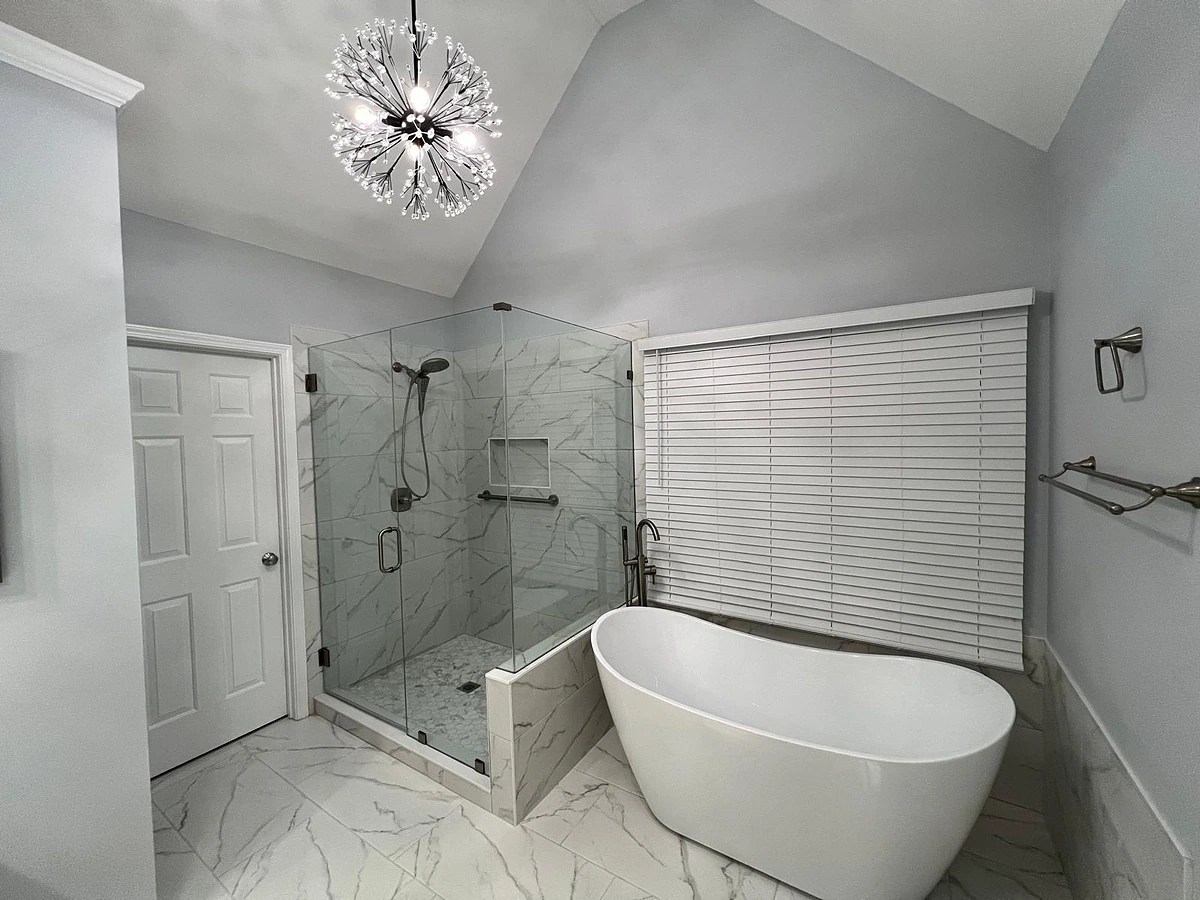 Freestanding soaking tub beside a marble walk-in shower under a modern chandelier