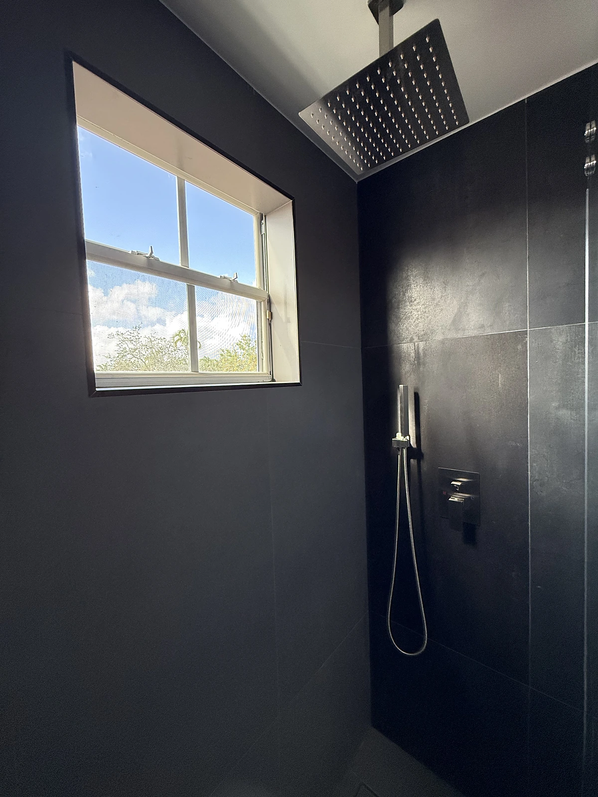 Dramatic black tile shower with rain head and window