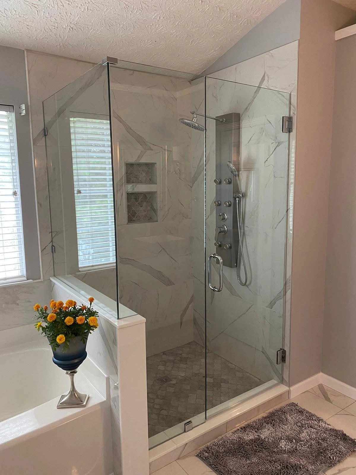 Corner glass shower with marble walls and mosaic floor