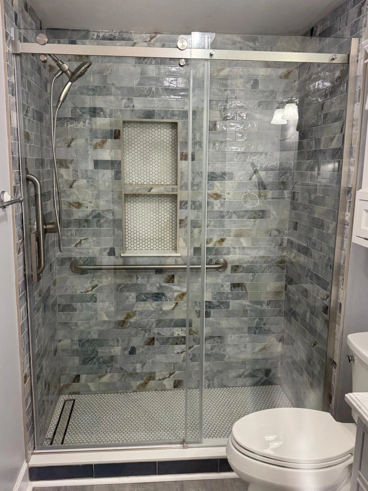 Glass-enclosed shower with green slate tile and built-in niche in a Broward County home
