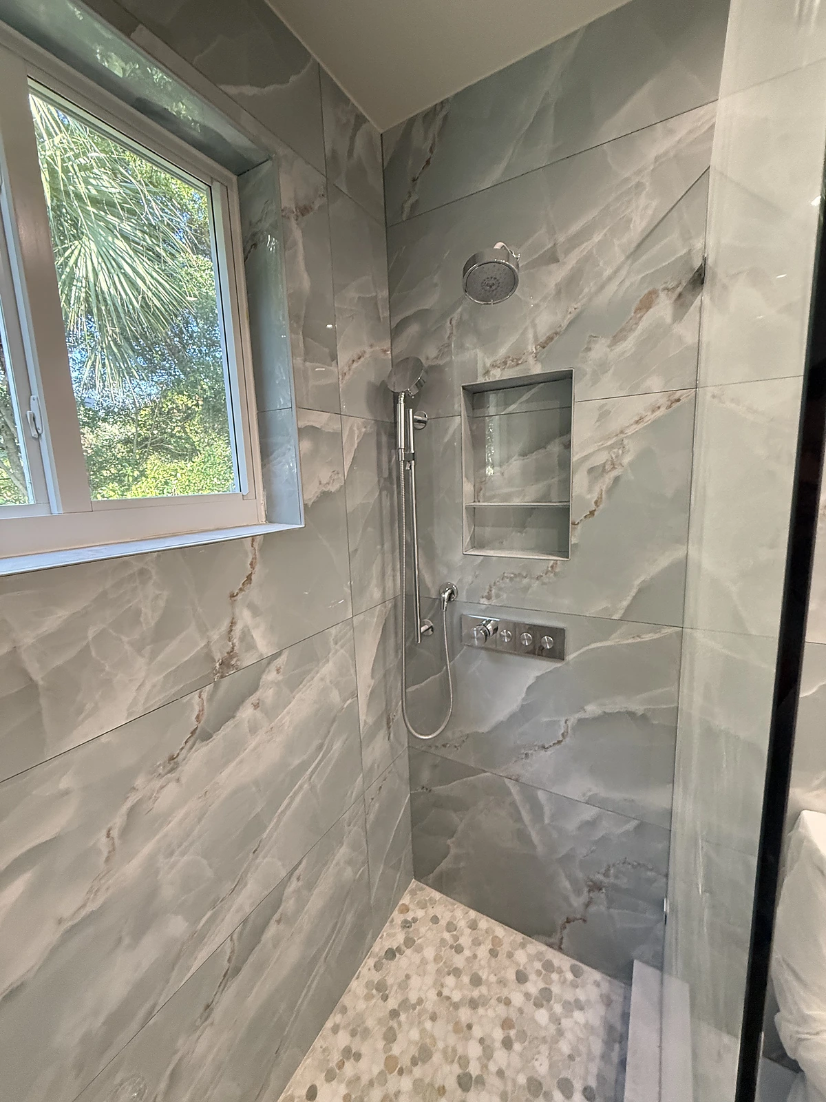 Grey stone-look tile shower with window and pebble accent floor