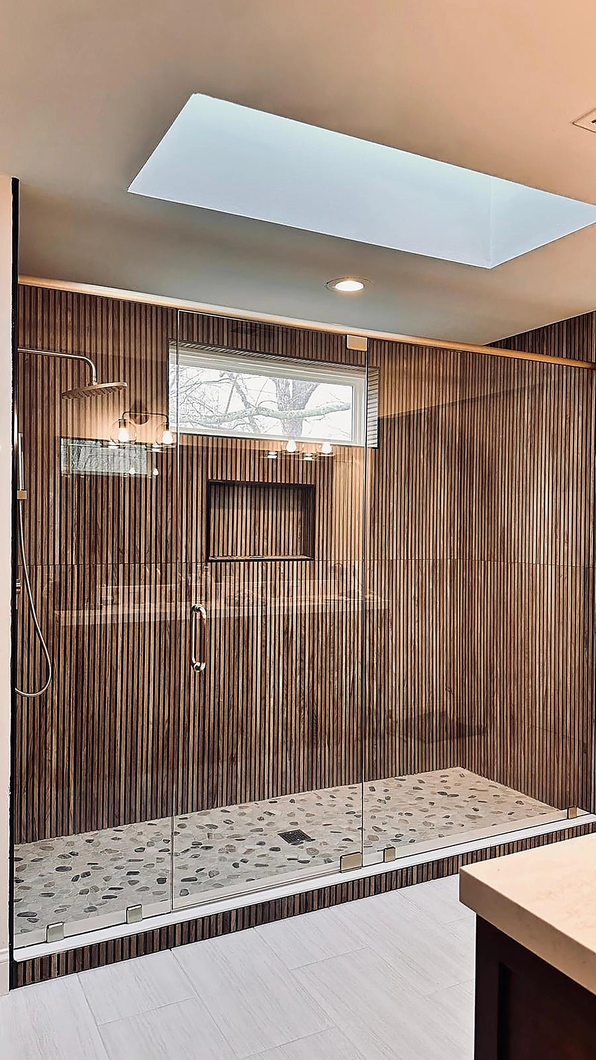 Wide walk-in shower in ribbed wood-look tile beneath a skylight
