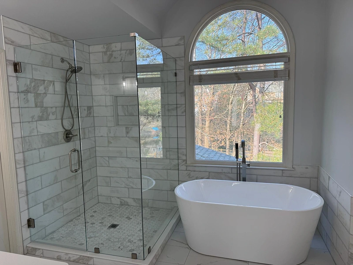 Subway tile shower and freestanding tub beneath an arched window