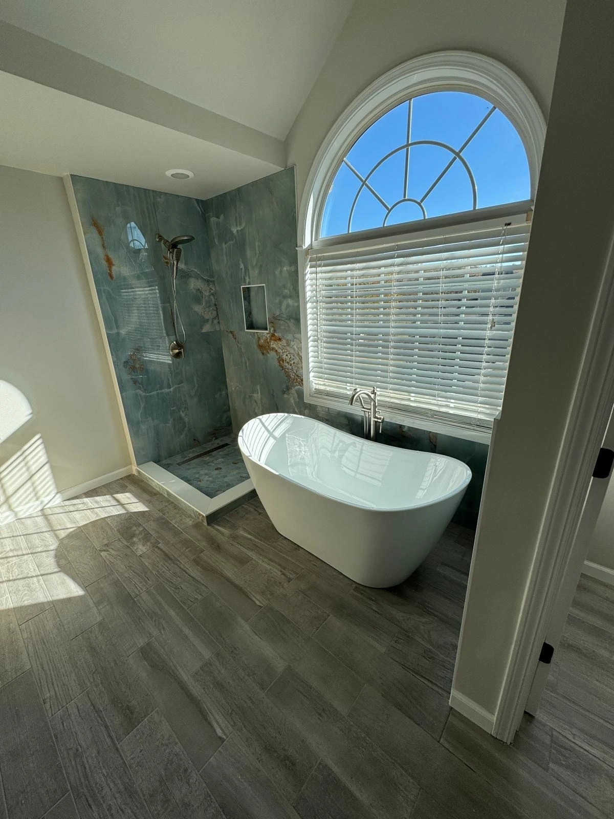 Freestanding tub beside a green marble walk-in shower