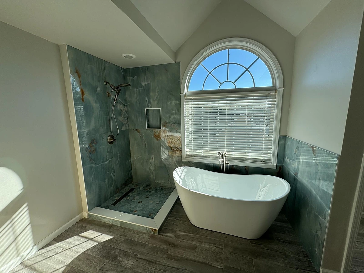 Freestanding tub and green tile shower under an arched window