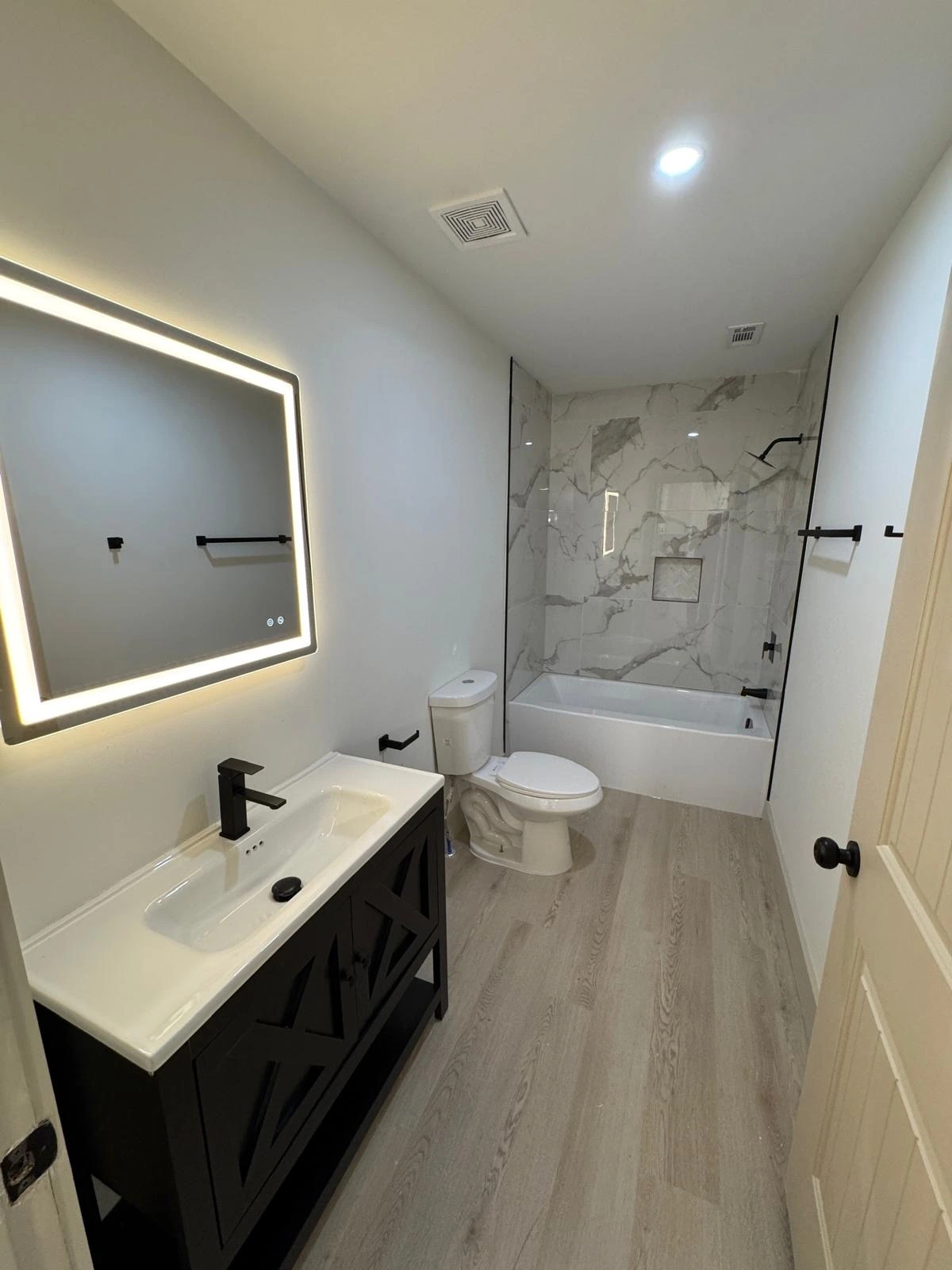 Compact bathroom remodel with marble tub-shower surround and black vanity — Weston, FL