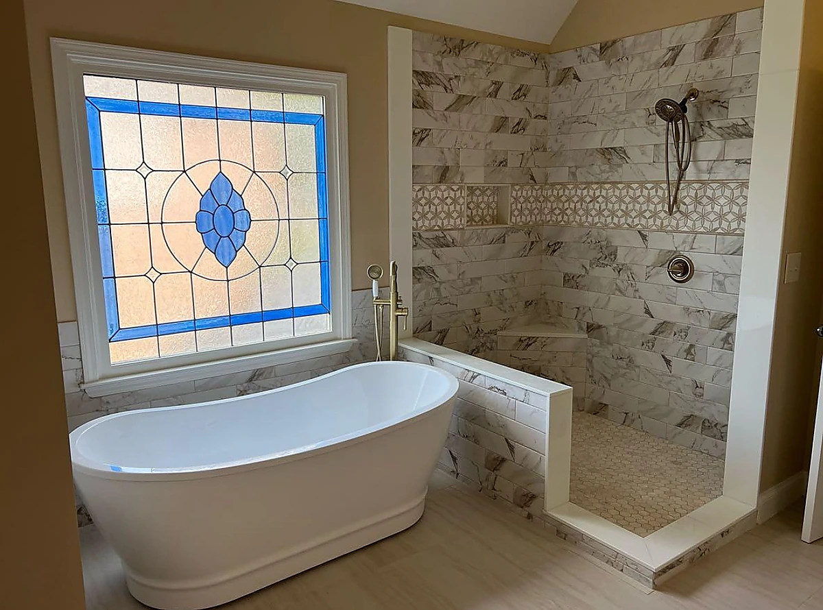 Freestanding tub beside a stained glass window and tiled shower