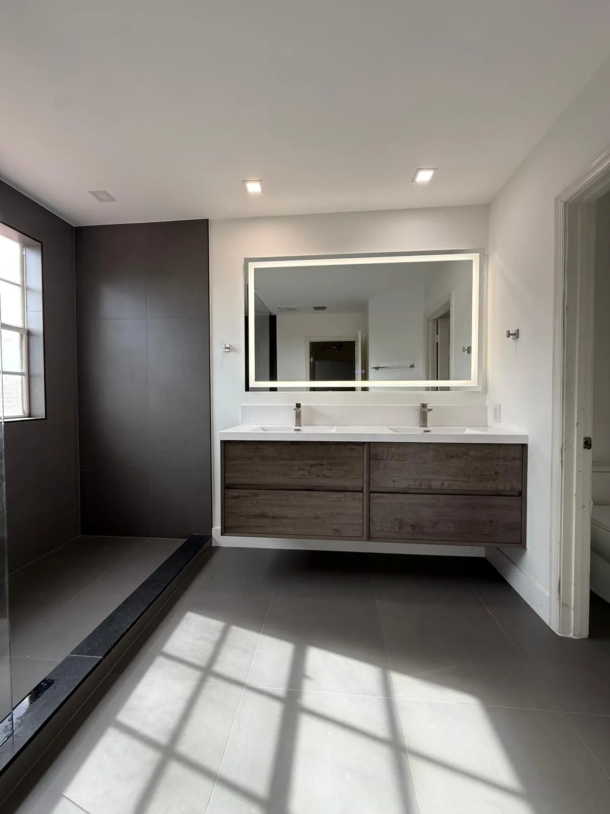 Floating wood vanity with backlit mirror in a sunlit bathroom