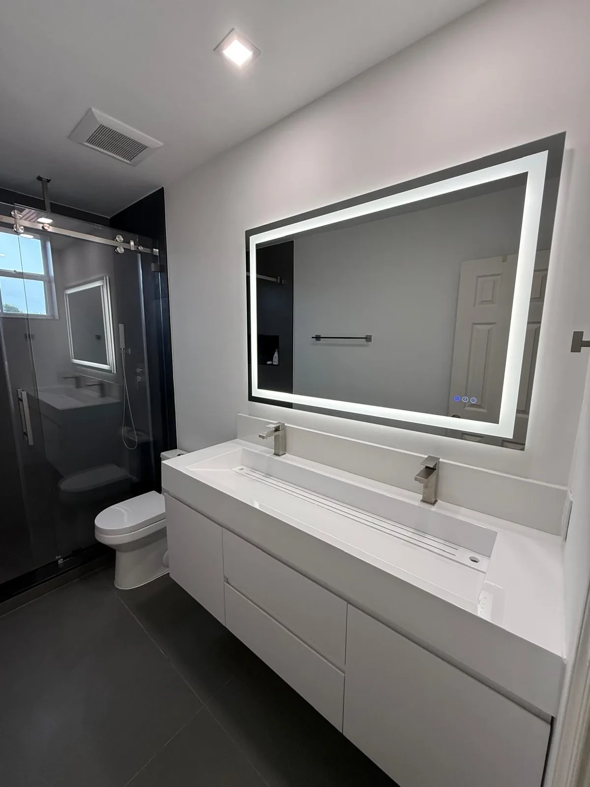 Compact bathroom with backlit mirror, white vanity and dark shower